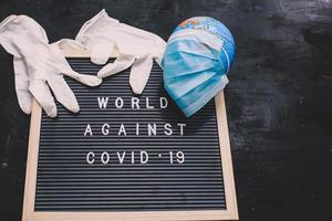 la citation sur le tableau des lettres dit que le monde contre le covid 19 avec des gants en caoutchouc et un globe terrestre dans un masque médical photo