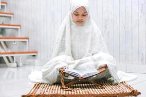 les jeunes musulmans asiatiques religieux lisent le livre sacré al-quran sur le tapis de prière à la maison. photo