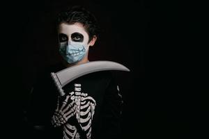 joyeux halloween, enfant portant un masque médical dans un costume de squelette avec une faux photo