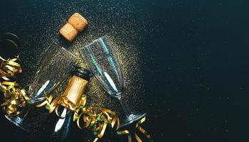 bonne année. bouteille de champagne avec deux verres, banderoles dorées et paillettes scintillantes avec espace de copie. fond de concept de célébration du nouvel an photo