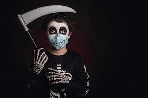 Joyeux Halloween. enfant portant un masque médical dans un costume de squelette avec une faux photo
