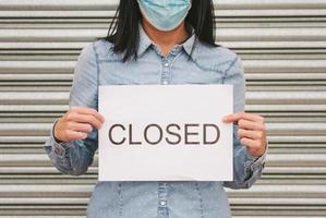 coronavirus.femme avec masque médical tenant un carton blanc avec le texte fermé photo