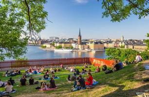 les jeunes passent du temps à s'asseoir, à boire, à manger sur la pelouse avec de l'herbe verte et des arbres autour de l'île de sodermalm photo