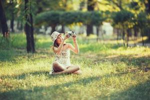 petite fille est jouée par un appareil photo assis sur l'herbe dans le parc. faire selfie et photographier le monde autour