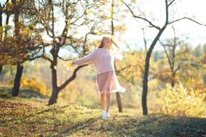 portraits d'une charmante fille rousse avec un joli visage. fille posant dans le parc d'automne dans un pull et une jupe de couleur corail. dans les mains d'une fille une feuille jaune photo