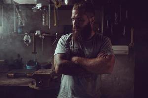 bel homme brutal avec une barbe debout dans son garage sur fond d'outils de réparation photo