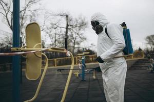 nettoyage et désinfection sur le terrain de jeu dans le complexe de la ville au milieu de l'épidémie de coronavirus équipes pour les efforts de désinfection prévention et contrôle des infections de la combinaison et du masque de protection épidémique photo