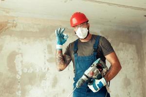 un constructeur avec un perforateur pose sur le fond d'un mur avec un espace vide à partir du texte le constructeur est vêtu d'une combinaison de protection et d'un casque photo