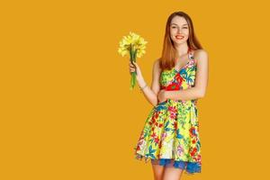 jeune femme contre le mur jaune avec des fleurs à la main photo