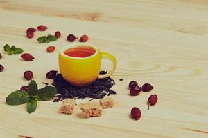 tasse de thé avec des roses de la hanche, sur une table en bois. une tasse faite de vrai citron photo