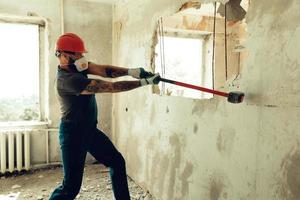 le constructeur avec un marteau dans les mains brise le mur de ciment le constructeur est vêtu d'une combinaison de protection et d'un casque photo