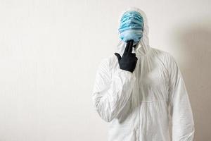 un homme en tenue de protection accroché avec des masques médicaux posant sur un fond de mur montrant divers gestes avec ses doigts photo