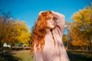portraits d'une charmante fille rousse avec un joli visage. fille posant dans le parc d'automne dans un pull et une jupe de couleur corail. la fille a une humeur merveilleuse photo