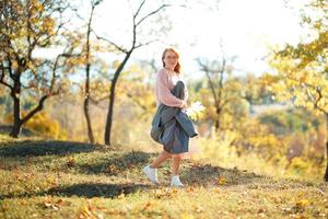 portraits d'une charmante fille rousse avec un joli visage. fille posant dans le parc d'automne dans un pull et une jupe de couleur corail. la fille a une humeur merveilleuse photo