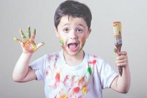 enfant drôle avec de la peinture et un pinceau sur un mur blanc photo