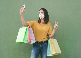 jeune femme heureuse portant un masque médical tenant un sac à provisions prenant un selfie sur smartphone photo