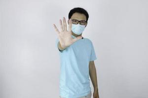 le jeune homme asiatique porte un masque hygiénique a peur ou panique avec la main d'arrêt gesticulant. peur d'une infection à coronavirus ou de maladies respiratoires comme la grippe. homme indonésien isolé sur fond blanc photo