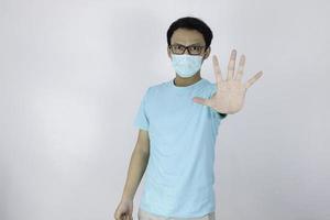 le jeune homme asiatique porte un masque hygiénique a peur ou panique avec la main d'arrêt gesticulant. peur d'une infection à coronavirus ou de maladies respiratoires comme la grippe. homme indonésien isolé sur fond blanc photo