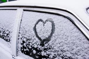 coeur dessiné sur un pare-brise de voiture recouvert de neige fraîche de noël photo