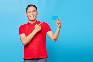 portrait d'un jeune homme asiatique joyeux pointant le doigt sur la carte de crédit isolé sur fond bleu photo