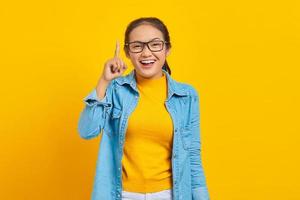 portrait d'une jeune étudiante asiatique joyeuse en vêtements denim ayant une idée créative et pointant le doigt vers le haut isolé sur fond jaune. éducation au concept d'université collégiale