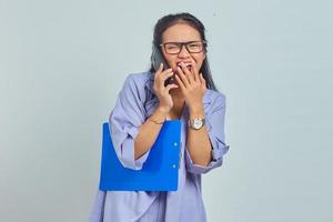 portrait d'une jeune femme asiatique joyeuse riant tout en parlant au téléphone portable avec des amis de quelque chose de drôle tout en tenant un dossier de documents isolé sur fond violet photo