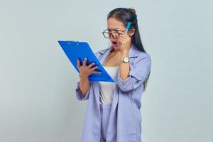 portrait d'une jeune femme d'affaires asiatique surprise regardant la liste d'emplois sur le presse-papiers isolé sur fond violet photo