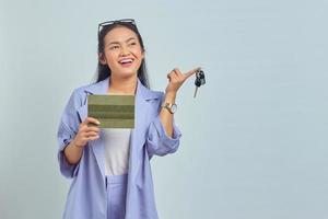 portrait d'une jeune femme asiatique joyeuse montrant le livre du véhicule et tenant les clés du véhicule isolées sur fond blanc photo