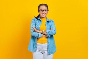 portrait d'une jeune étudiante asiatique souriante dans des vêtements en denim croisés sur la poitrine et l'air confiant isolé sur fond jaune. éducation au concept d'université collégiale photo