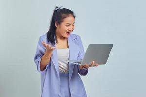 portrait d'une jeune femme asiatique souriante regardant un ordinateur portable et célébrant le succès de l'obtention d'un nouveau projet isolé sur fond blanc photo