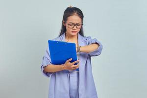 portrait de jeune femme asiatique vérifiant l'heure sur la montre et tenant le presse-papiers isolé sur fond violet photo