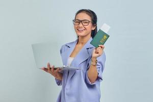 portrait de jeune femme asiatique debout à l'aide d'un ordinateur portable et tenant un livre de passeport avec une expression joyeuse isolée sur fond blanc photo