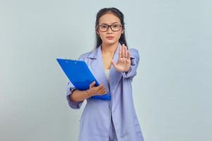 portrait d'une jeune femme asiatique en colère tenant un dossier et dit non montre un geste d'interdiction refuse quelque chose d'isolé sur fond violet photo