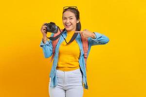 portrait d'une jeune femme asiatique souriante avec sac à dos et doigt pointant vers une caméra professionnelle isolée sur fond jaune photo