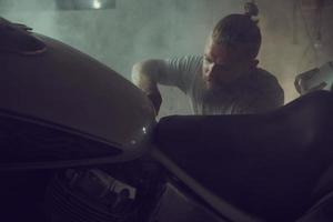 bel homme brutal avec une barbe réparant une moto dans son garage photo