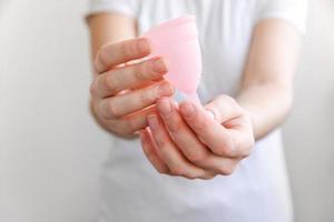 main de femme tenant une coupe menstruelle rose isolée sur fond blanc. femme alternative moderne éco hygiène gynécologique en période de menstruation. récipient pour le sang dans la main de la fille. photo