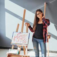 une fille peintre pensive créative peint une image colorée sur toile avec des couleurs à l'huile en atelier. photo