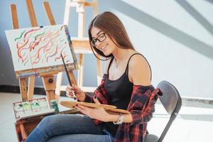 une fille peintre pensive créative peint une image colorée sur toile avec des couleurs à l'huile en atelier. photo