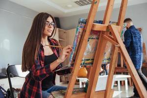 une fille peintre pensive créative peint une image colorée sur toile avec des couleurs à l'huile en atelier. photo