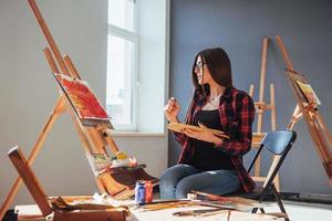 artiste aux cheveux noirs tenant un pinceau à la main et dessine une image sur toile. pense que tirer sur photo