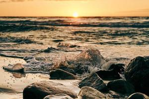 soleil jaune presque à l'horizon sur la mer d'un bleu profond, vue atmosphérique depuis la plage de la mer rocheuse photo