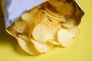 les hanches de pommes de terre sur fond jaune, les croustilles sont un en-cas dans un sac emballé dans du plastique prêt à manger et de la nourriture grasse ou de la malbouffe photo