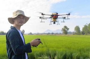 jeune agriculteur intelligent contrôlant la pulvérisation d'engrais et de pesticides par drone sur les terres agricoles, les innovations de haute technologie et l'agriculture intelligente photo