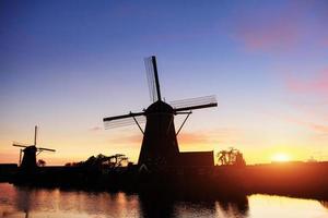 paysage avec beau moulin hollandais traditionnel près des cours d'eau avec coucher de soleil fantastique et reflet dans l'eau. Pays-Bas. photo