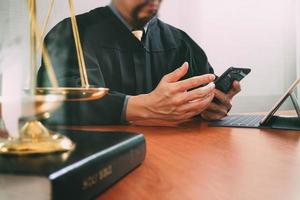 concept de justice et de droit.juge masculin dans une salle d'audience avec le marteau et travaillant avec un téléphone intelligent et une balance en laiton sur une table en bois photo