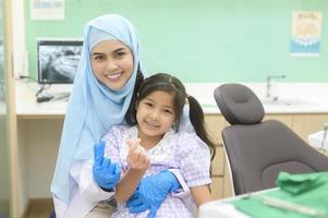 une petite fille mignonne ayant des dents examinées par un dentiste musulman dans une clinique dentaire, un contrôle des dents et un concept de dents saines photo