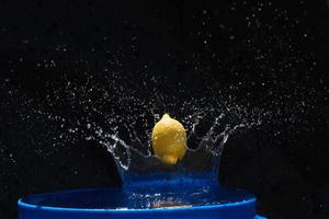 citron jaune tombant dans l'eau bleue sur fond noir photo