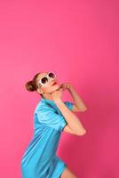 portrait de jeune belle femme en robe de soie bleue et lunettes de soleil blanches sur fond rose photo