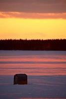 cabane de pêche sur glace sur un lac gelé au coucher du soleil photo