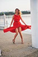 heureuse belle jeune femme dansant de liberté en été avec lac en arrière-plan. contraste des couleurs rouge et blanc
